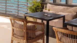 A terrace with wicker furniture, a table with a glass of wine, and a view of the ocean. - White Exclusive Suite & Villas (Lagoa)