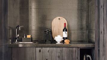 Una cocina compacta con armarios de madera oscura, un lavamanos, una botella de vino y una cafetera.