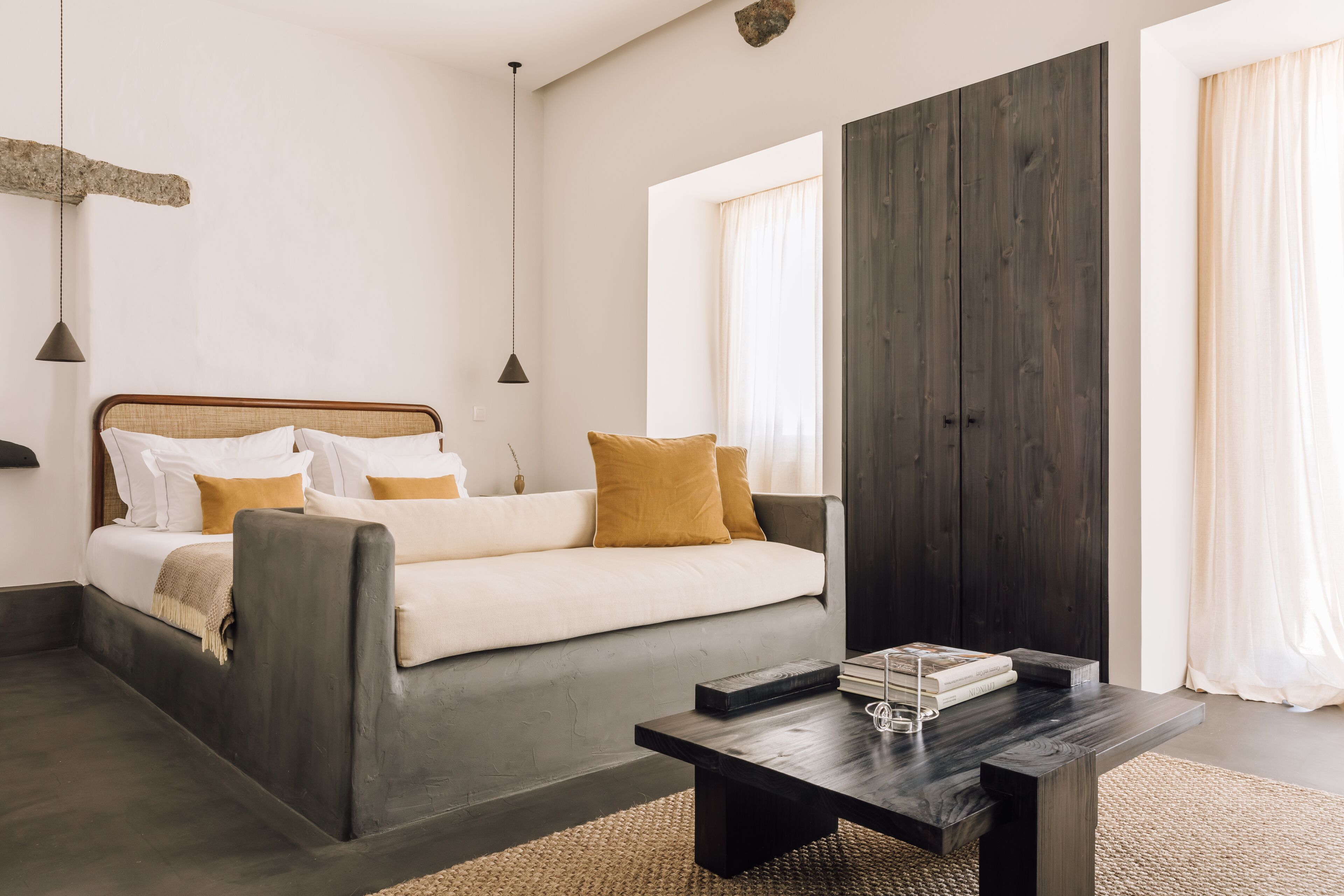 A modern bedroom with a bed, a dark wooden accent wall, a large window, and a coffee table.