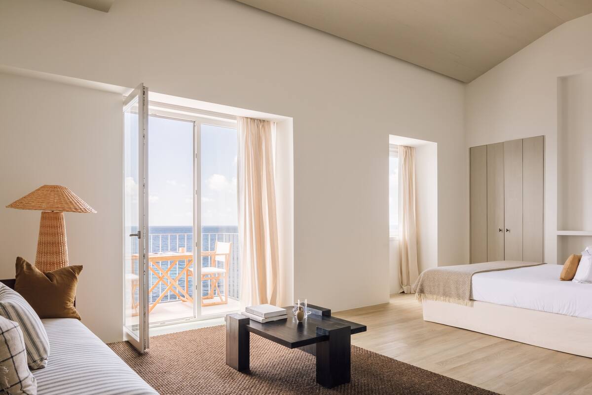 A spacious room with a bed, a sofa, a table, and a balcony with a view of the sea.