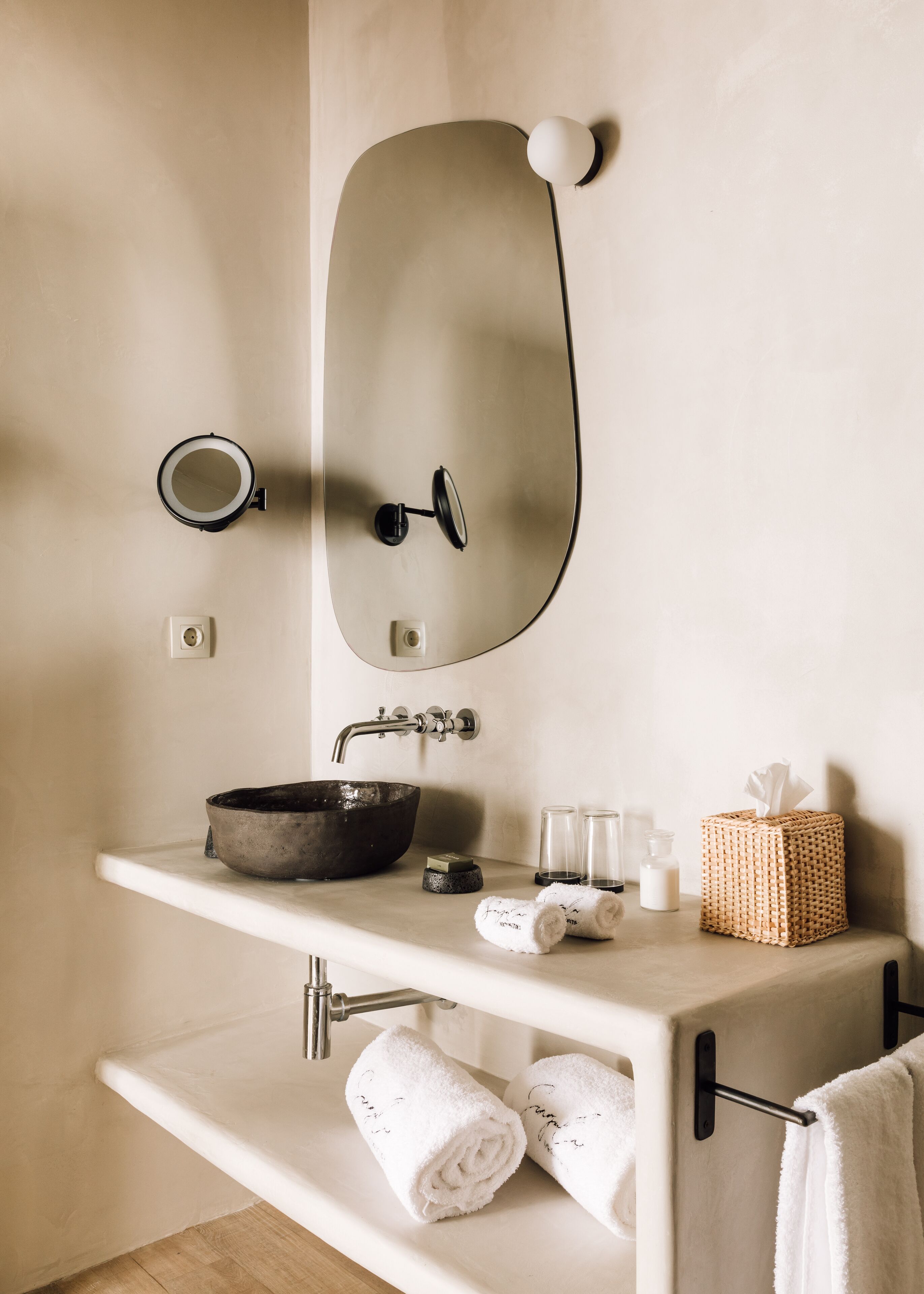 Une salle de bain avec un grand miroir, un lavabo rond, un receveur noir, un porte-serviettes avec des serviettes, un petit panier et un savonnière.