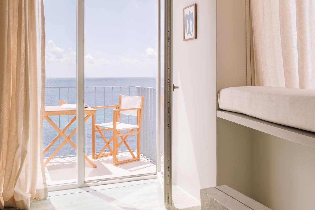 A room with a balcony, a bed, and a wooden floor.