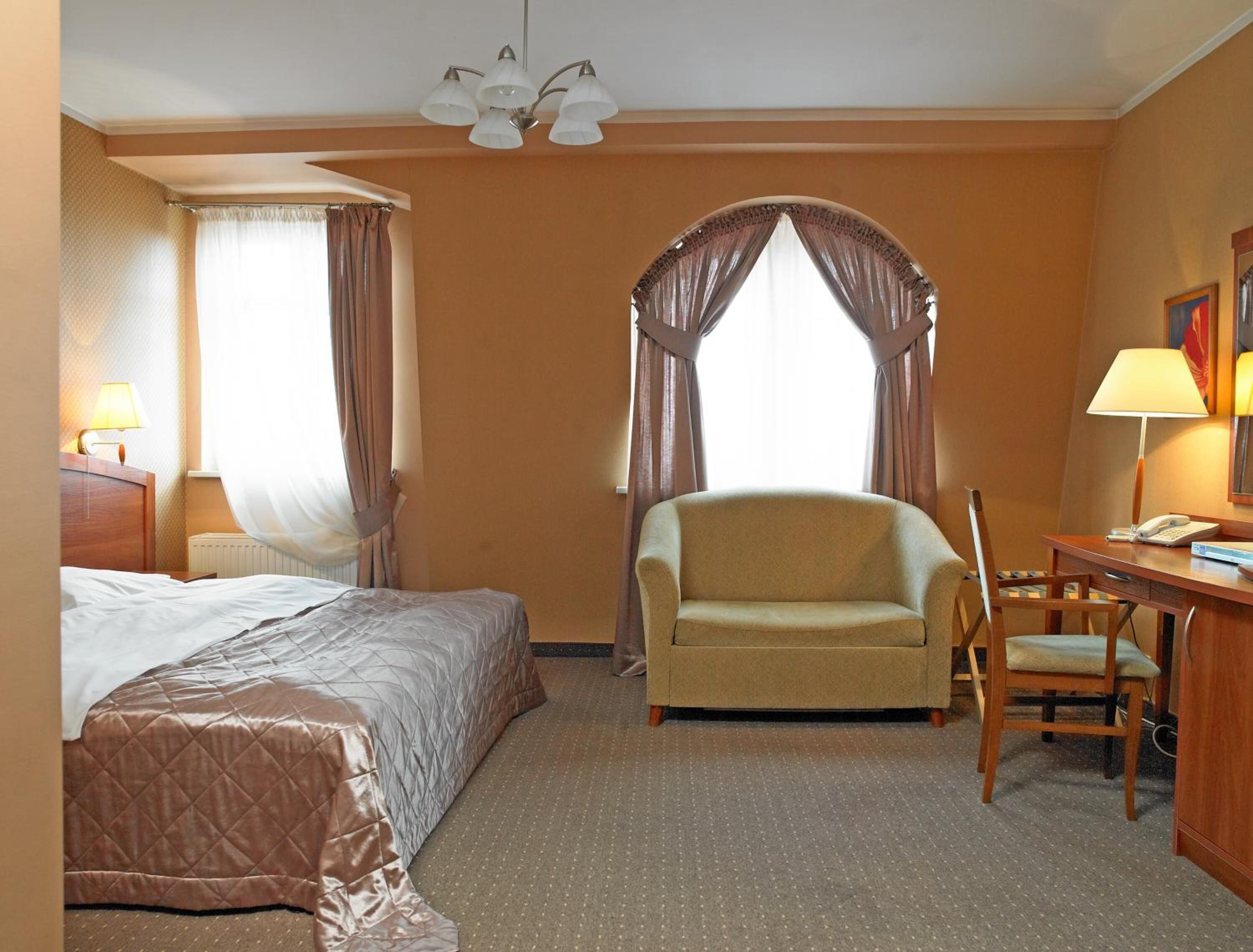 Una habitación de hotel con una cama, una silla, un escritorio y una lámpara.