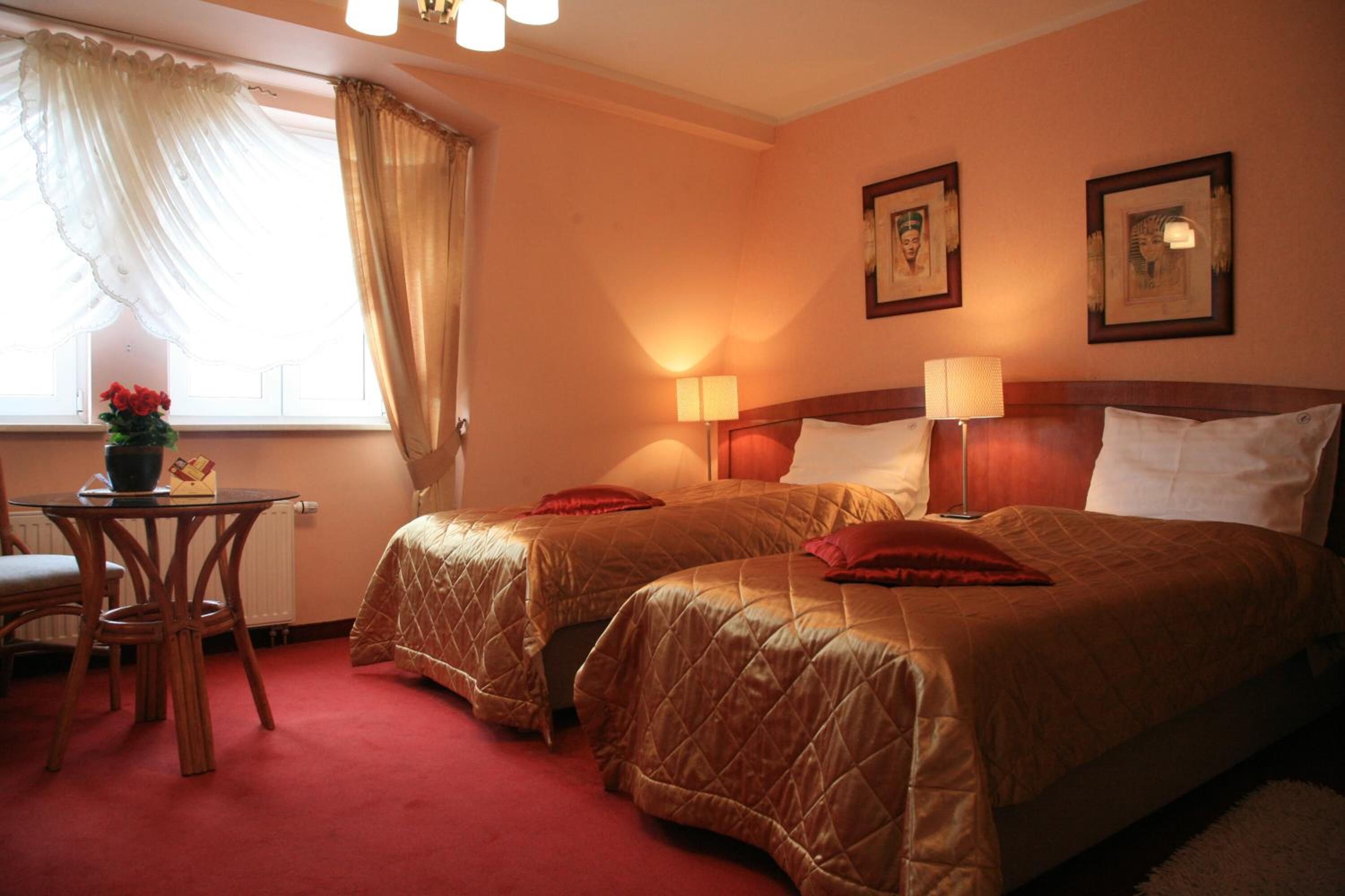 Una habitaci ón de hotel con dos camas, una mesita con una silla y un ventanal con cortinas.