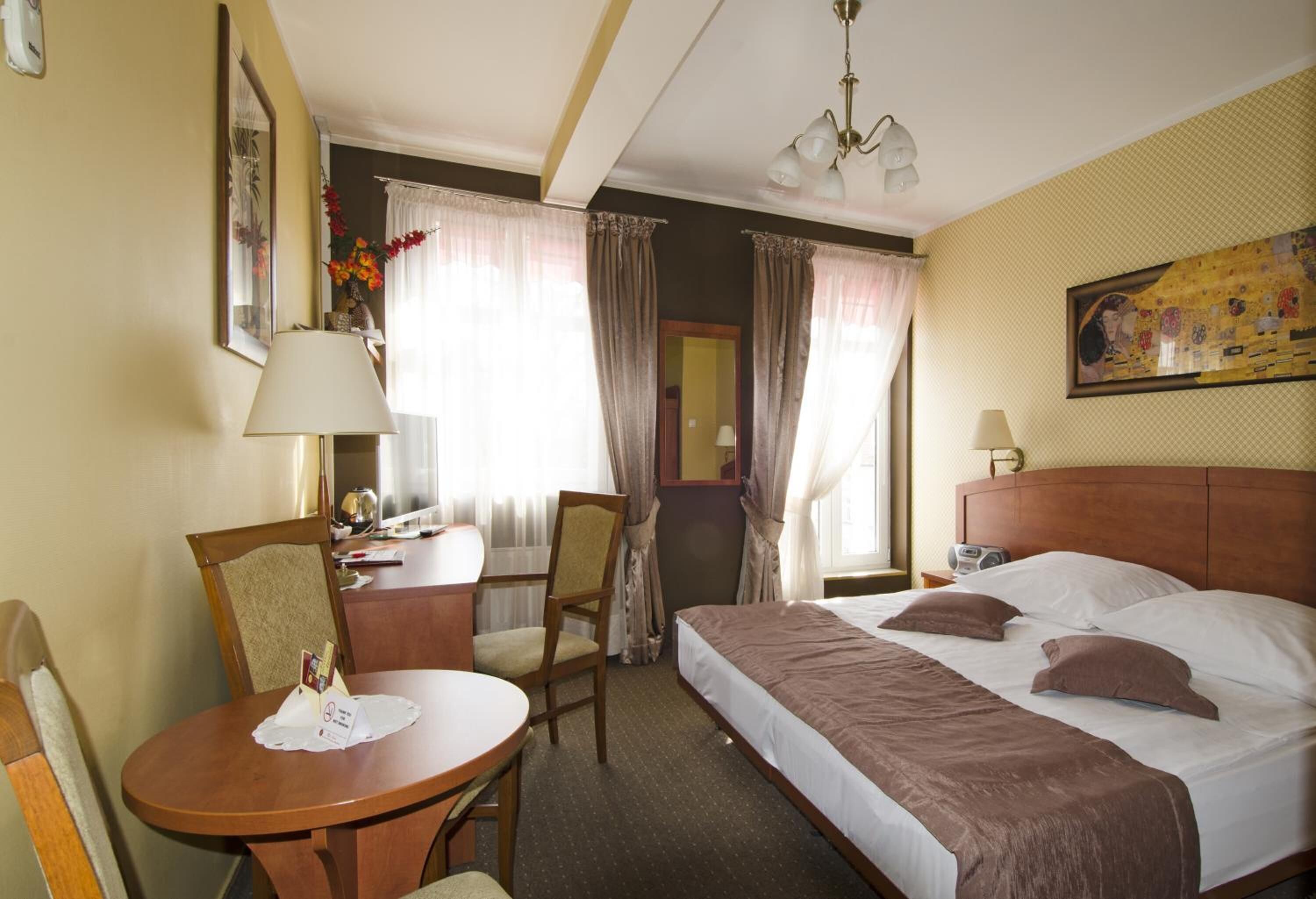 A hotel room with a single bed, a desk with a chair, a small table, and a chair.