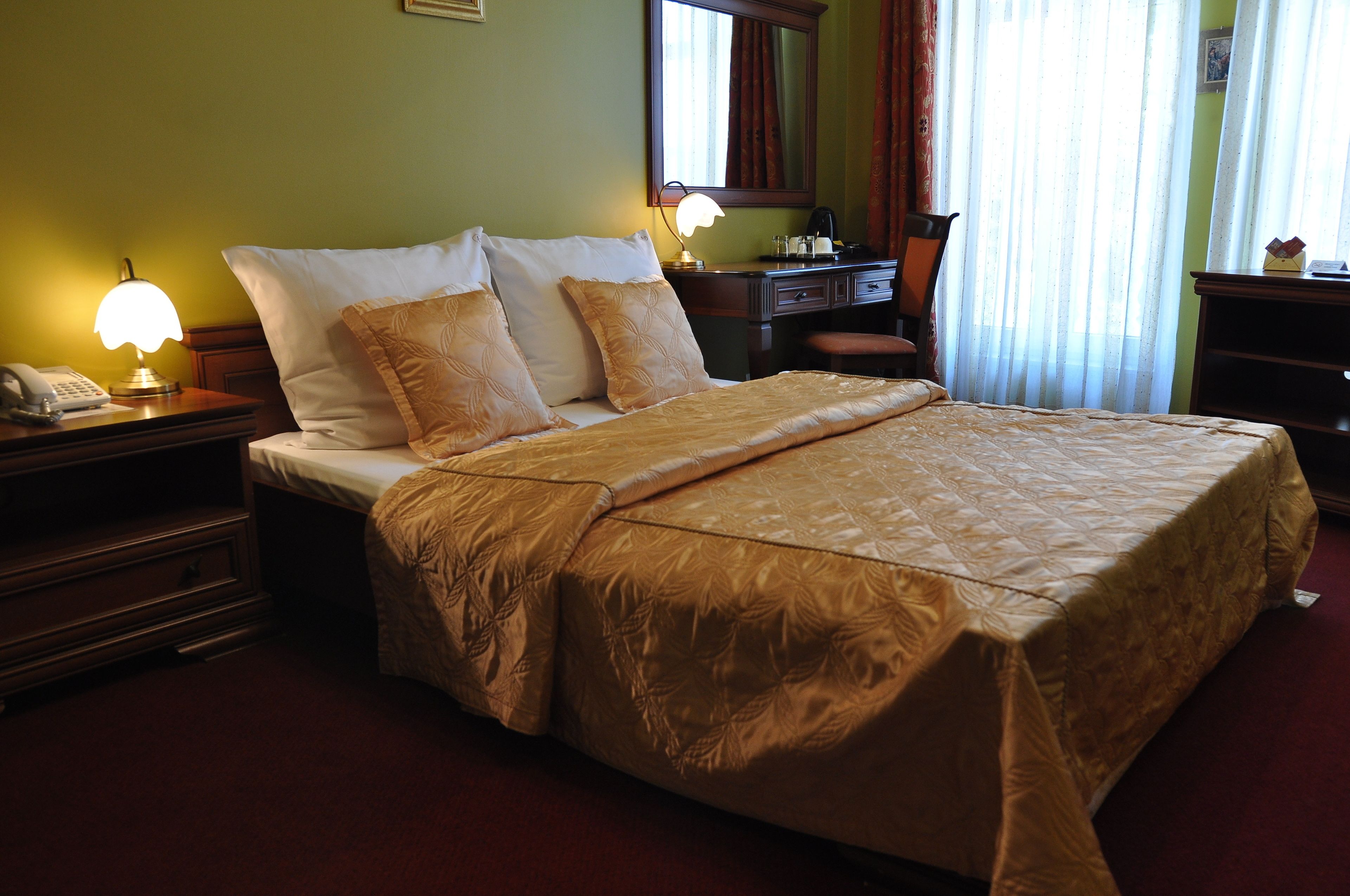 A hotel room with a large bed, a nightstand with a lamp, a desk, and a chair.