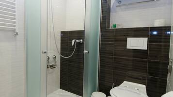 Et moderne badeværelse med et brusebad bag glas, et toilet og en håndklædestang.