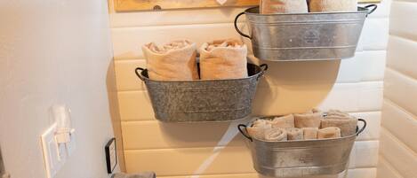 Un baño pequeño con un inodoro, un banco de madera y cubos metálicos con toallas.