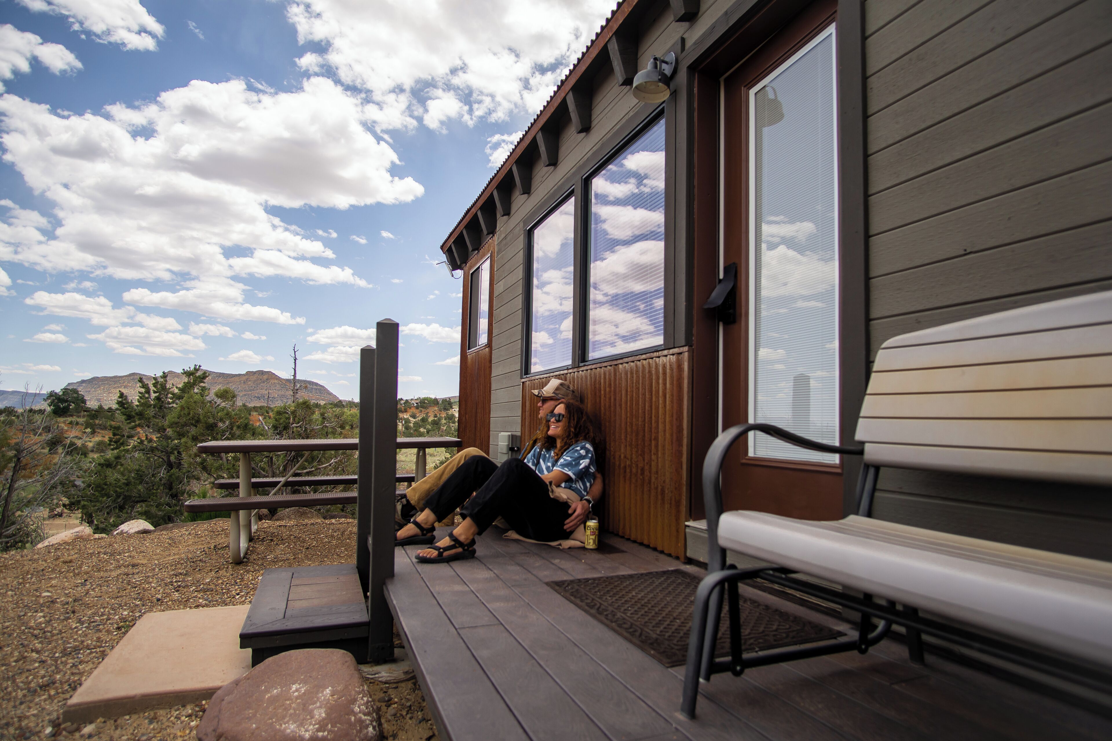A person sitting on a porch with a wooden bench and a picnic table.