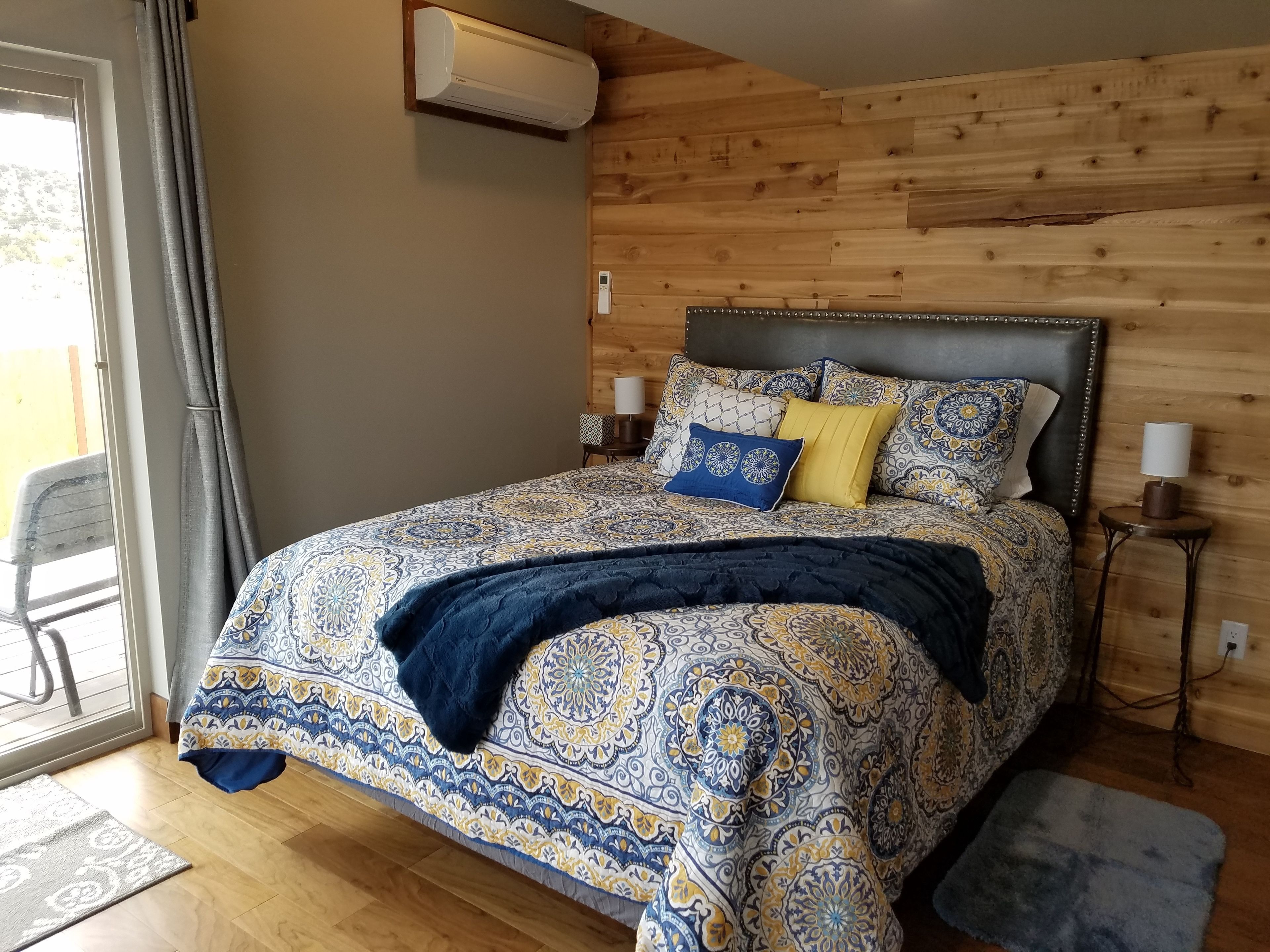 A bedroom with a patterned bedspread, a dark blue throw blanket, and a wooden headboard.