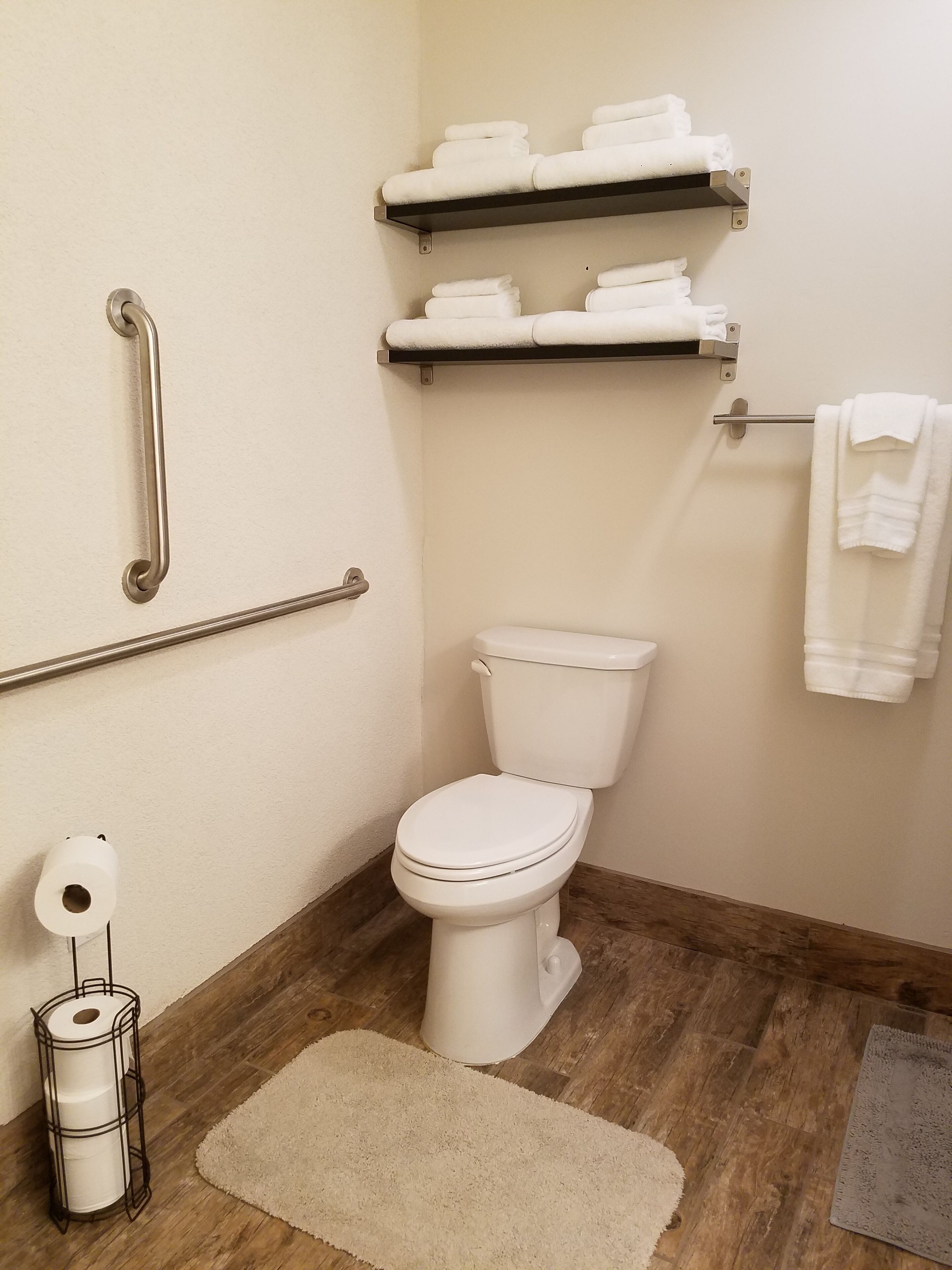 A bathroom with a toilet, grab bars, a towel rack, and a toilet paper holder.