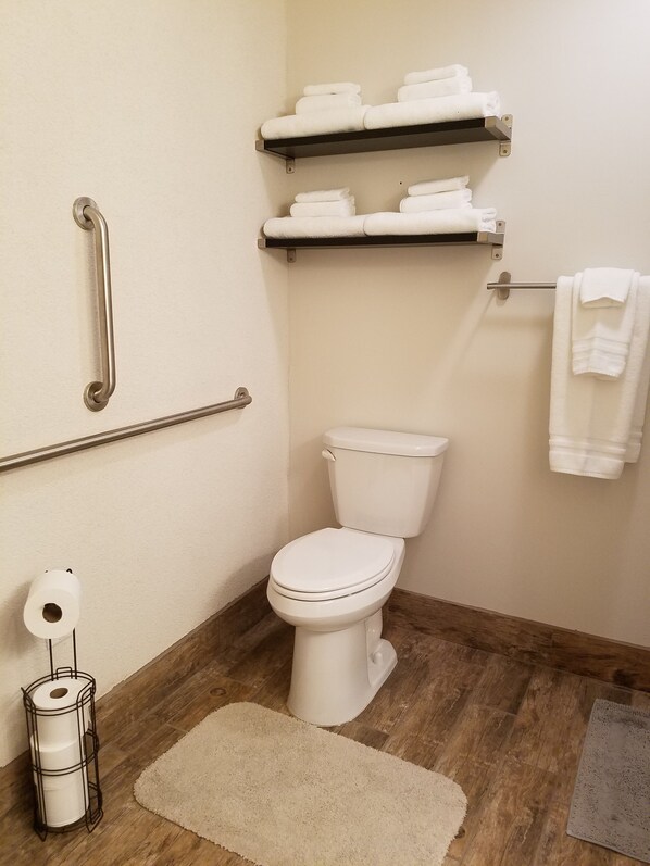 A bathroom with a toilet, grab bars, a towel rack, and a toilet paper holder. - Escalante Grand Resort (Escalante)