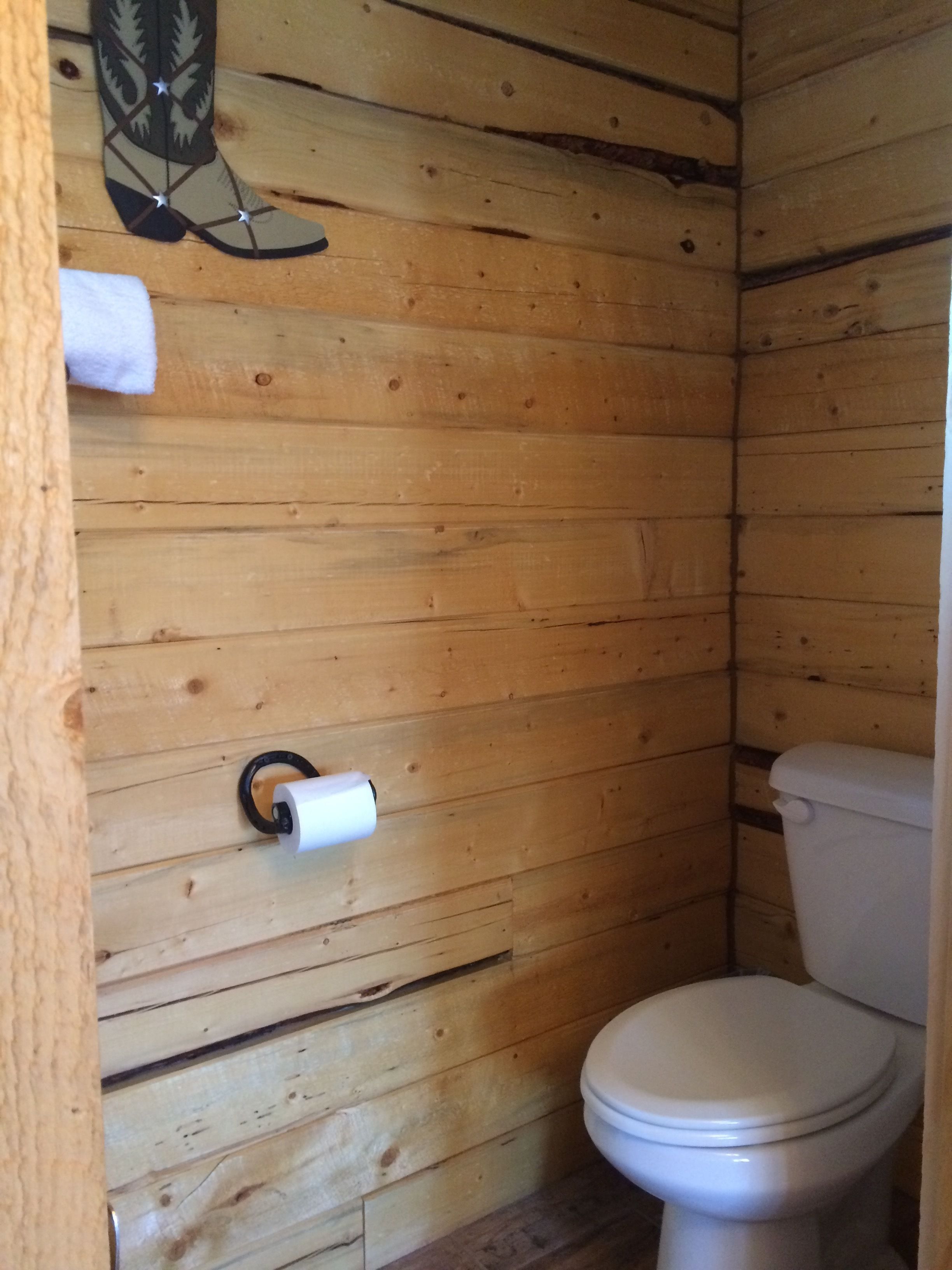 Une salle de bain aux murs lambrés, équipée de toilettes et d’un porte-rouleau de papier toilette.
