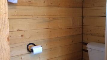 Une salle de bain aux murs lambrés, équipée de toilettes et d’un porte-rouleau de papier toilette.