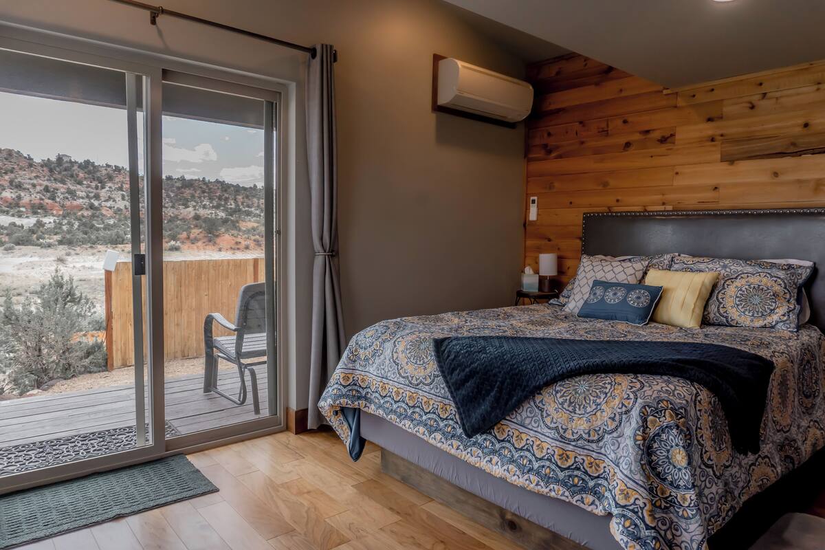 A bedroom with a large bed, a wooden headboard, a nightstand, and a view through a sliding glass door to an outdoor deck.