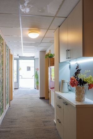 A hallway with a carpeted floor, a ceiling with a light fixture, and a counter with a coffee maker and a vase of flowers. - Smart2Stay Magnolia (Warsaw)