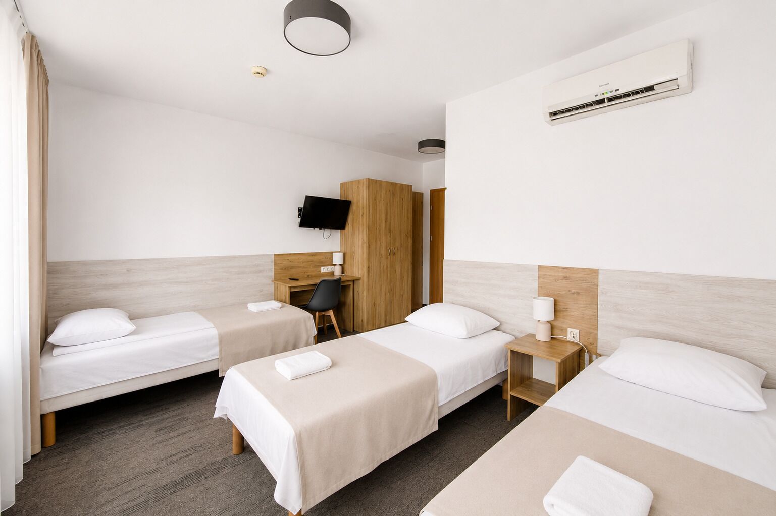 Ett hotellrum med två sängar, ett skrivbord, en stol, en TV och en luftkonditioneringsanläggning.