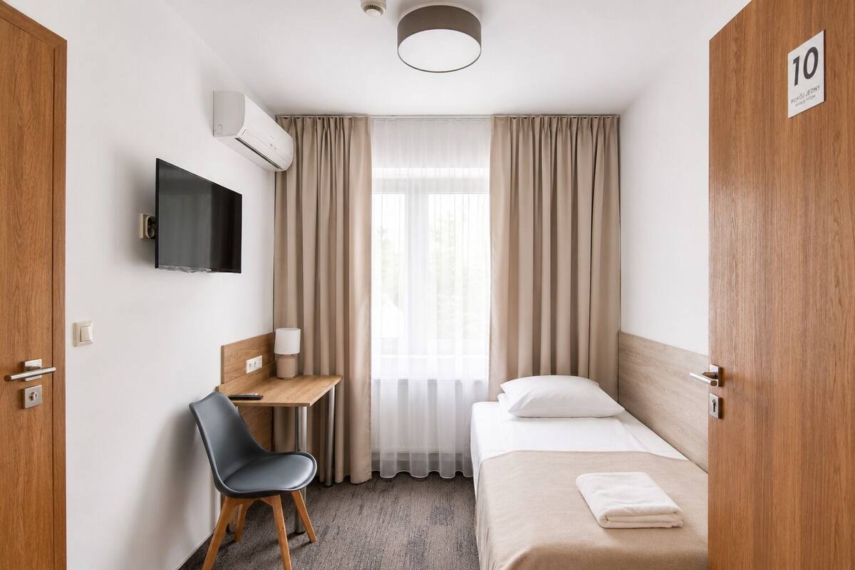 A hotel room with a bed, a desk with a chair, a TV, and a window with curtains.