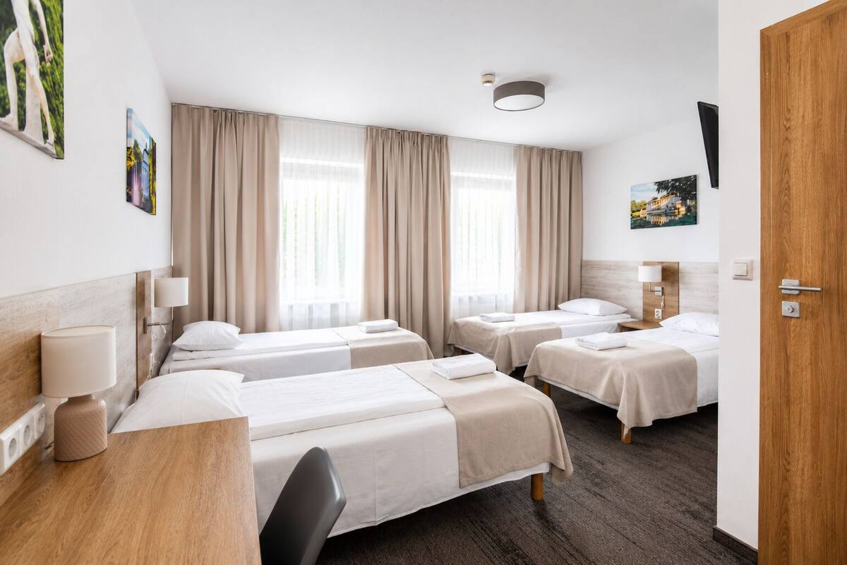 A hotel room with three beds, a desk, a chair, and a TV mounted on the wall.