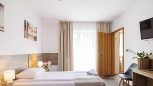 Hotellihuone, jossa on sänky, yöpöydät, työpöytä, tuoli, televisio ja ikkuna, jossa on verhot.