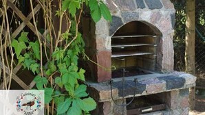A stone-built outdoor oven with a metal shelf, surrounded by greenery and a wooden fence. - Holiday Home Zgorzale by Lake Radunskie (Zgorzałe)