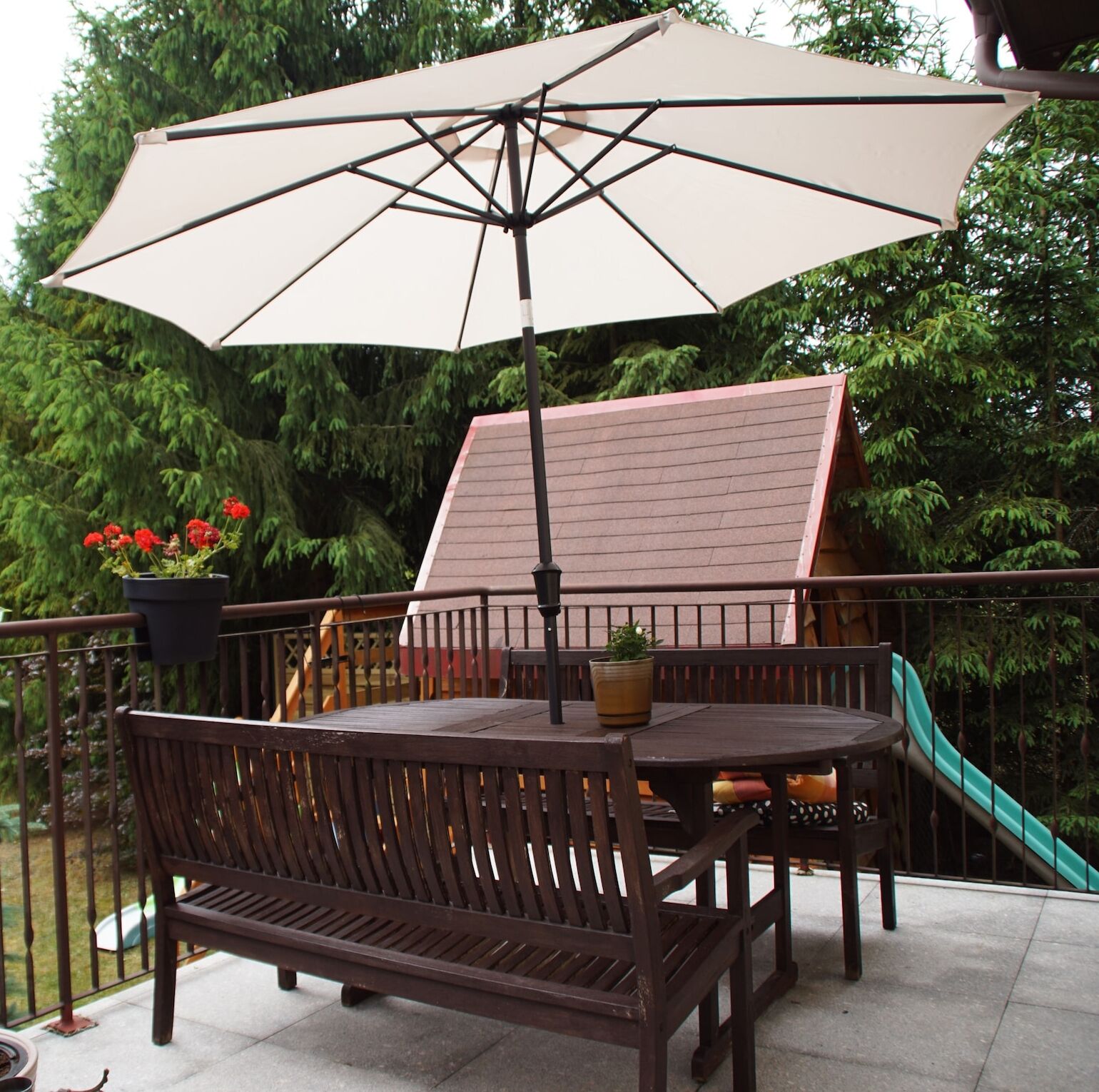 Un patio con tavolo e panchina in legno, un ombrellone e uno scivolo sullo sfondo.