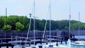A marina with boats docked, a wooden pier, and a forested hillside in the background. - Holiday Home Zgorzale by Lake Radunskie (Zgorzałe)