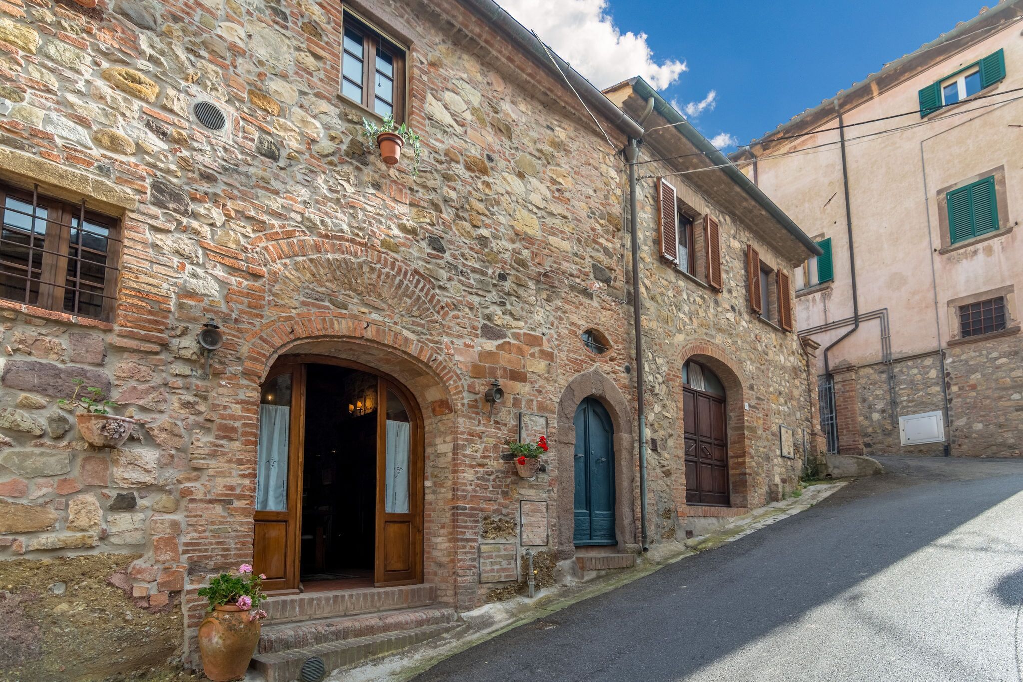 Ein Gebäude aus Stein mit Rundbögen und Fenstern, eine schmale Gasse und ein klarer Himmel.