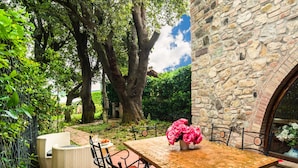 Un patio con pared de piedra, mobiliario de mimbre y una mesa con un jarrón de flores.