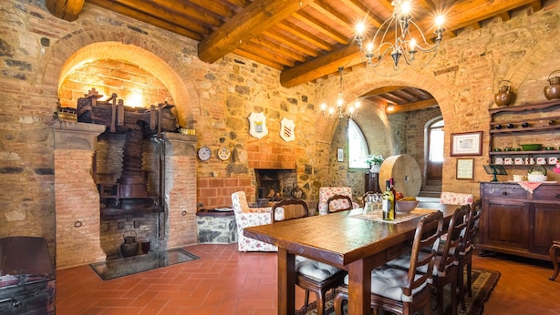 Un interior rústico de piedra con una mesa y sillas de madera, una chimenea y una araña.