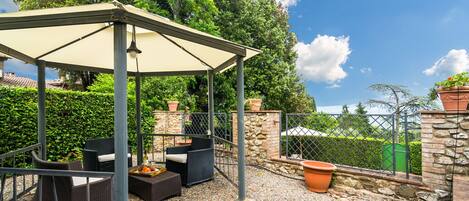 Un espace extérieur aménagé avec des meubles en osier et une pergola, le tout abrité.