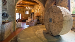 Una habitación de paredes de piedra con una gran piedra giratoria, vigas de madera y una chimenea.
