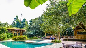 Un área de piscina con terraza de madera, sillas de descanso y una zona de estar cubierta.