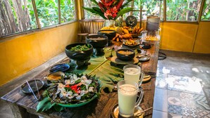 Una mesa de comedor con diversos platos y bebidas, rodeada de sillas y una ventana con vistas a zonas verdes.