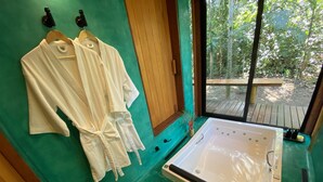 Una habitación con bañera, dos albornoces blancos colgados en un perchero y vistas al exterior a través de una ventana.