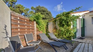 Une terrasse avec quatre chaises longues, une clôture en bois et un bâtiment blanc aux volets verts.
