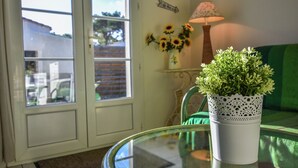 Une table en verre sur laquelle repose un pot blanc contenant des plantes vertes, une chaise verte, une lampe et une porte donnant sur l’extérieur.