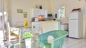 Une cuisine avec des meubles blancs, un four à micro-ondes, un grille-pain et un réfrigérateur. On y trouve une table à manger avec des chaises et un vase rempli de fleurs.
