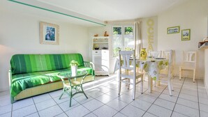 Une pièce avec un canapé à rayures vertes, une petite table sur laquelle est posée une plante en pot, et un coin repas avec une table et des chaises.