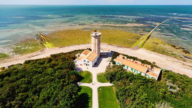 Vue aérienne d’une propriété située sur la côte, avec un phare, un bâtiment principal et une construction plus petite.