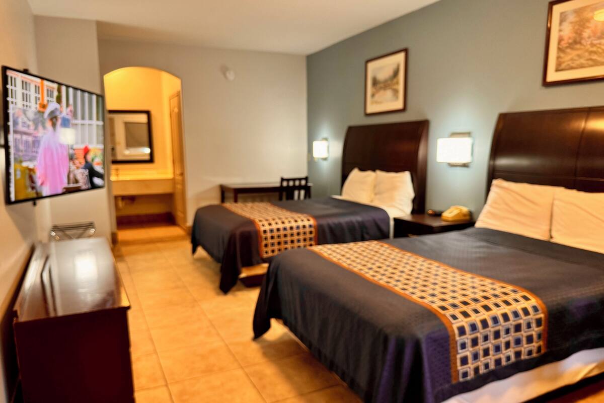A hotel room with two beds, a TV, a desk, and a chair.