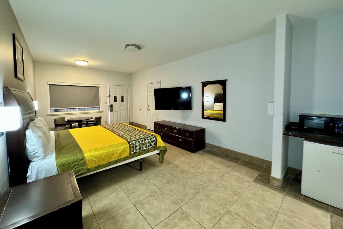 A hotel room with a bed, a desk, a TV, a mirror, and a kitchenette.