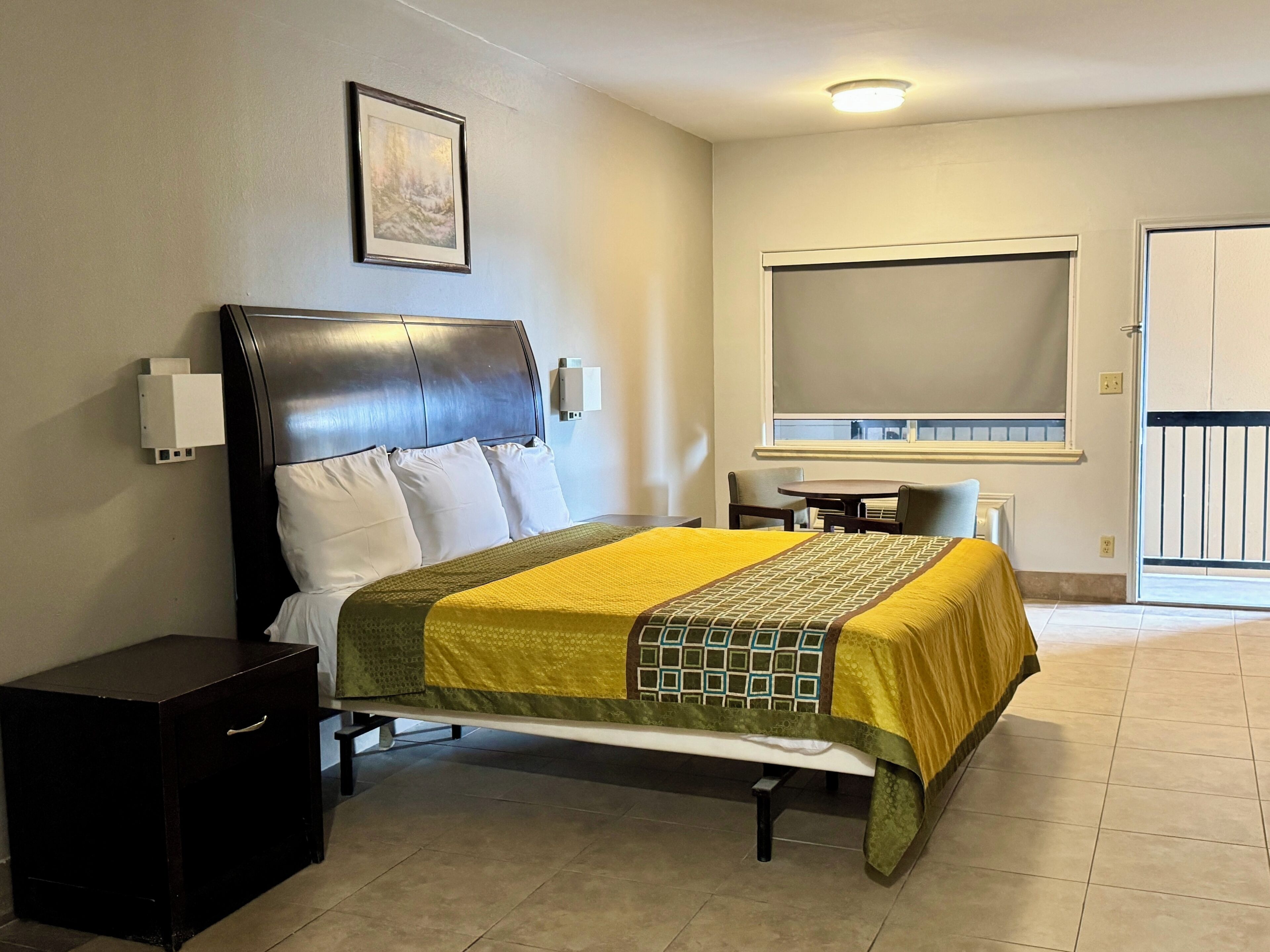 Una habitación de hotel con cama, mesita de noche, silla, ventana y puerta.