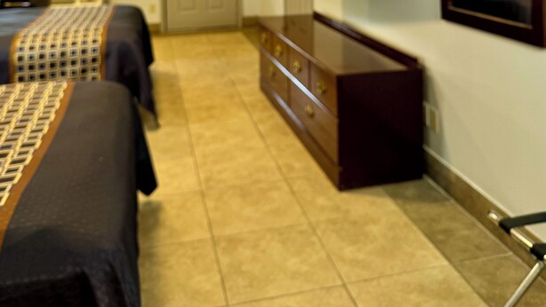 A hotel room with a bed, a dresser, a TV mounted on the wall, and a window with blinds.