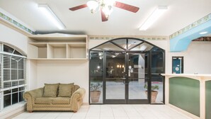 A hotel lobby with a beige sofa, a ceiling fan, a reception desk, and a glass door leading to the outside.