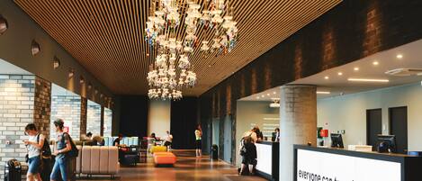 A modern lobby with a central chandelier, a reception desk, and seating areas.