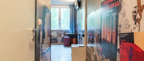 A corridor with posters on the walls, a window with curtains, and a door with a handle.