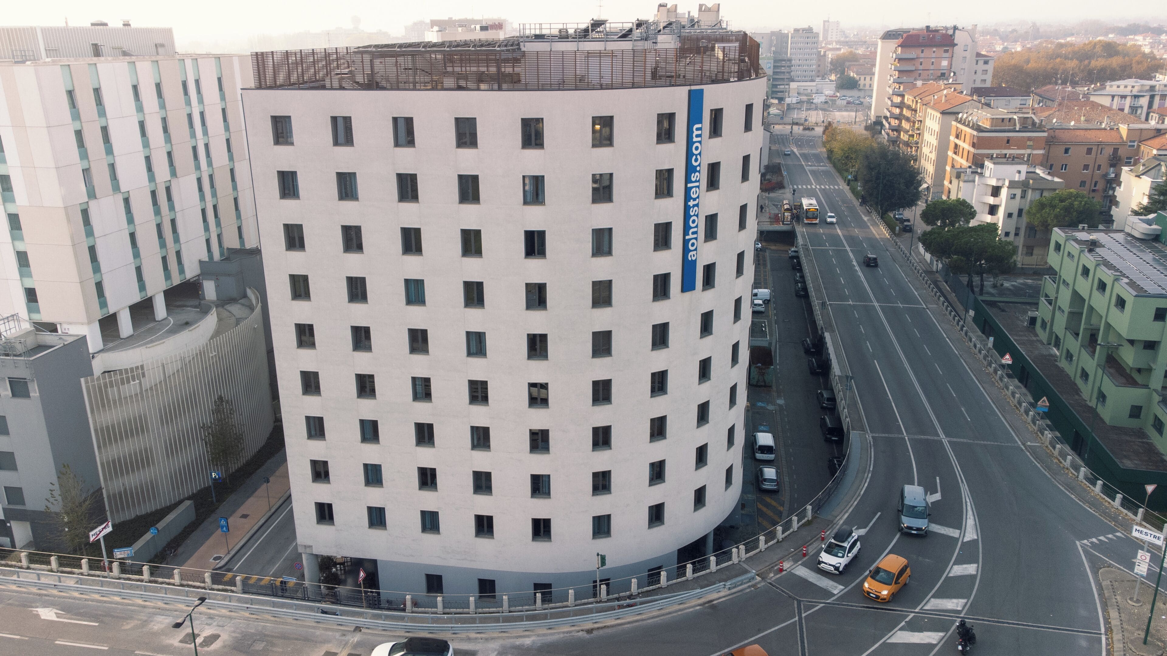 A modern building with a curved facade, multiple windows, and a blue vertical sign.