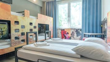 Quarto de hotel com beliches, janela com cortinas e obras de arte nas paredes.