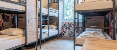 A dormitory room with bunk beds, a wooden table, and a window with a view of trees.